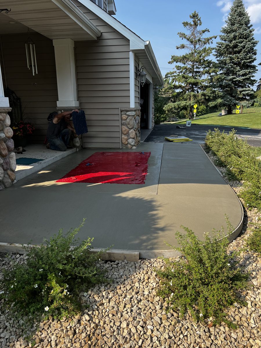Curved concrete front entry walkway freshly finished at a stone-accented entrance