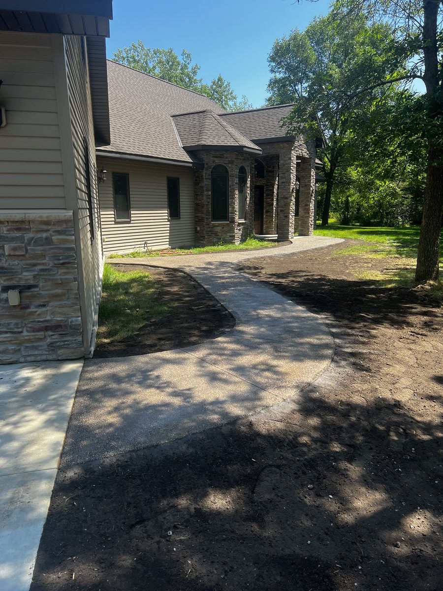 Curved concrete walkway leading to a stone-columned front entry