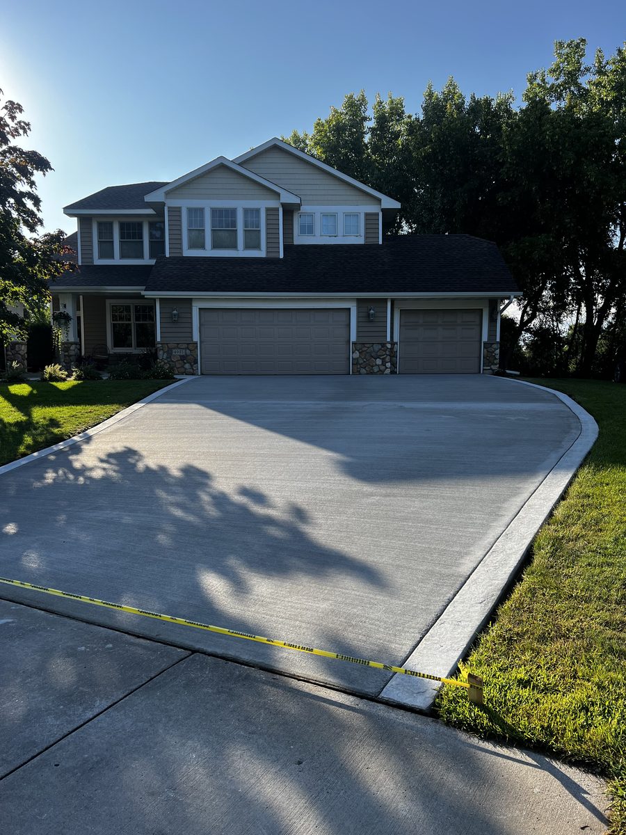 Wide broom-finish concrete driveway curving to a three-stall garage