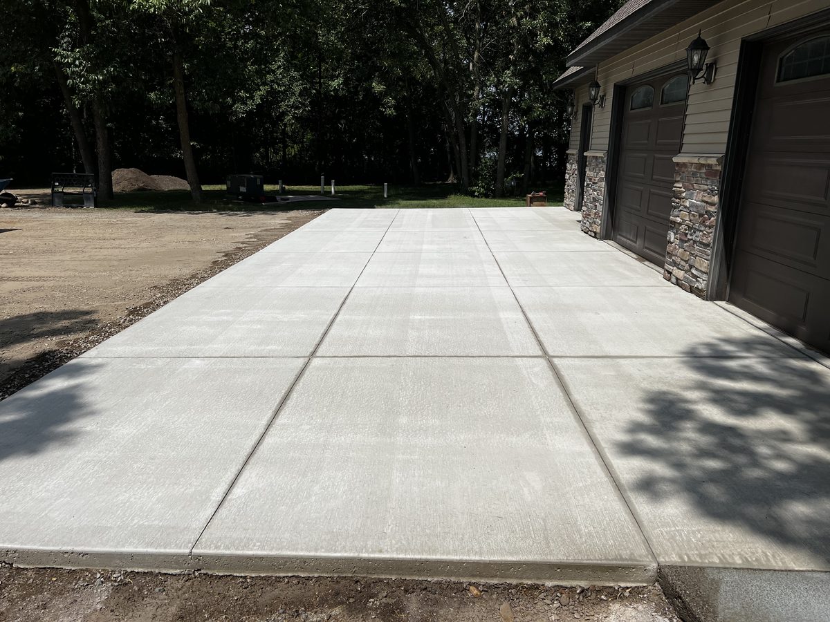 Wide concrete driveway with cut control joints leading to a stone-accented garage