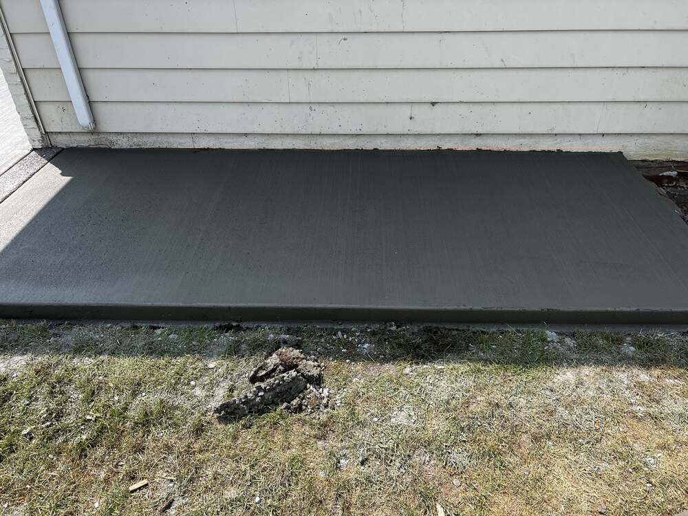 Freshly poured broom-finish concrete sidewalk section along a home, level and uniform
